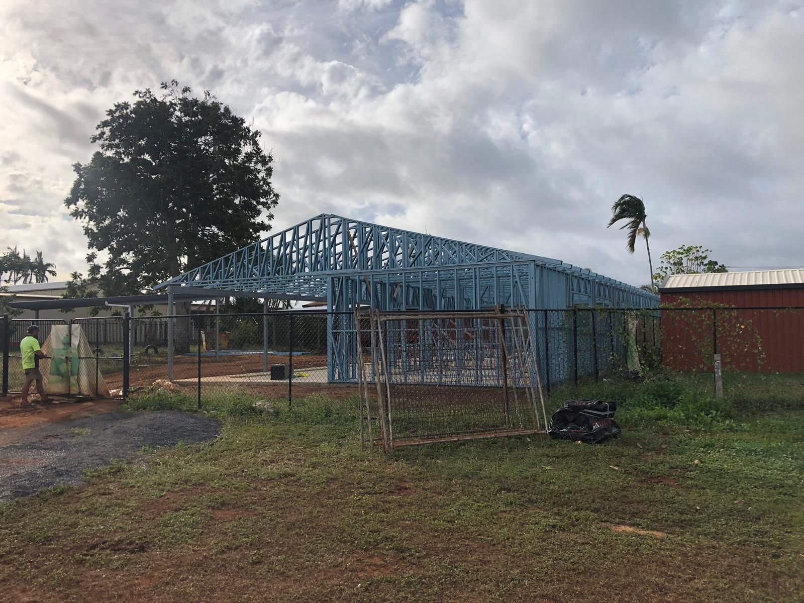 Steel frame construction of a building, surrounded by a fence, under cloudy skies.