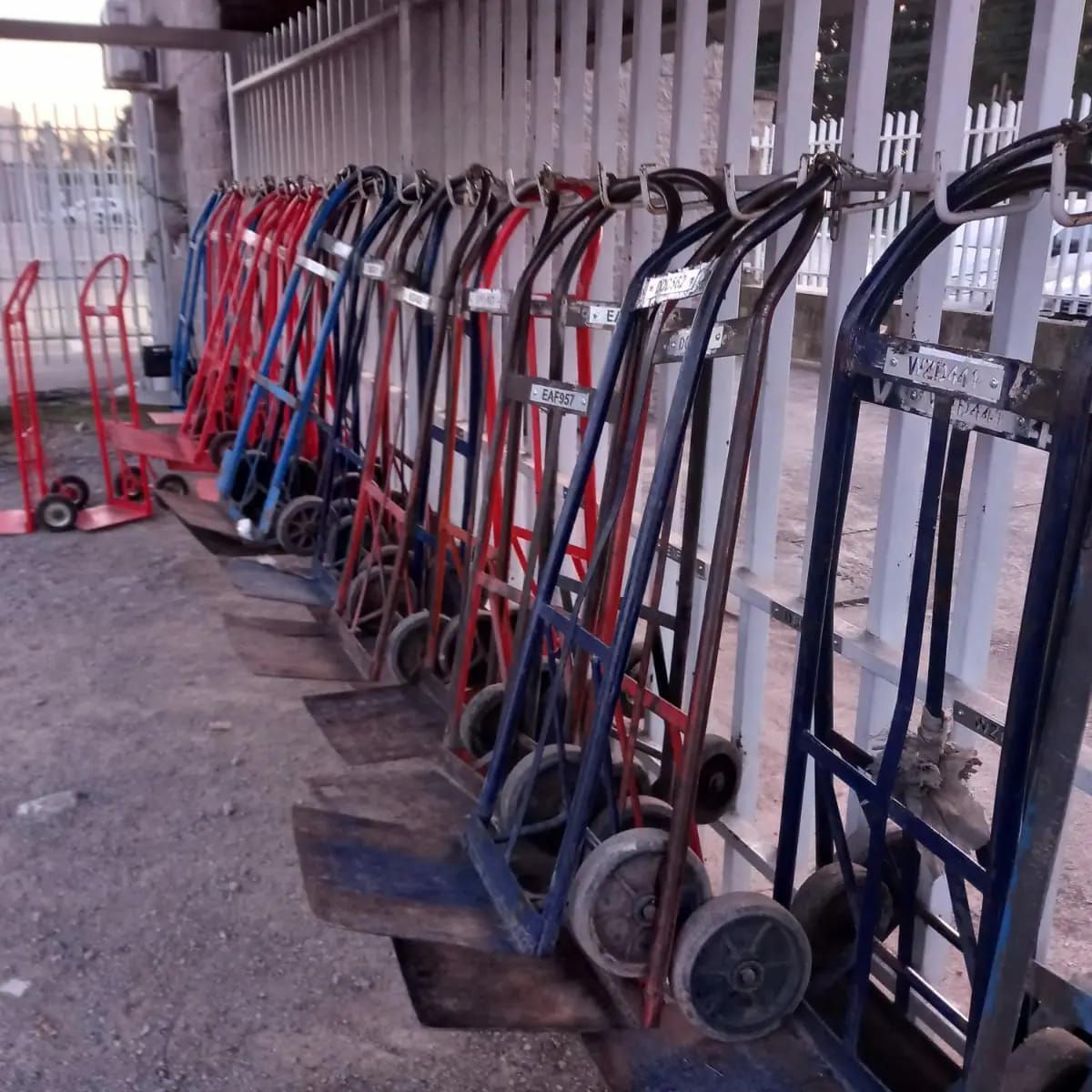 Carretillas manuales de varios colores (rojo, azul) alineadas a lo largo de una valla.