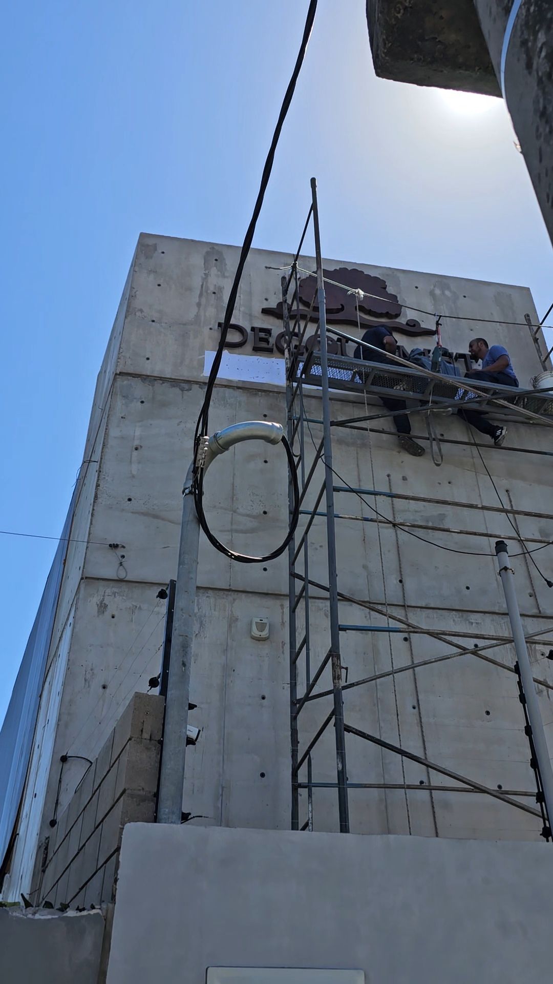 Obreros de la construcción en andamios, trabajando en un edificio de hormigón bajo un cielo soleado.