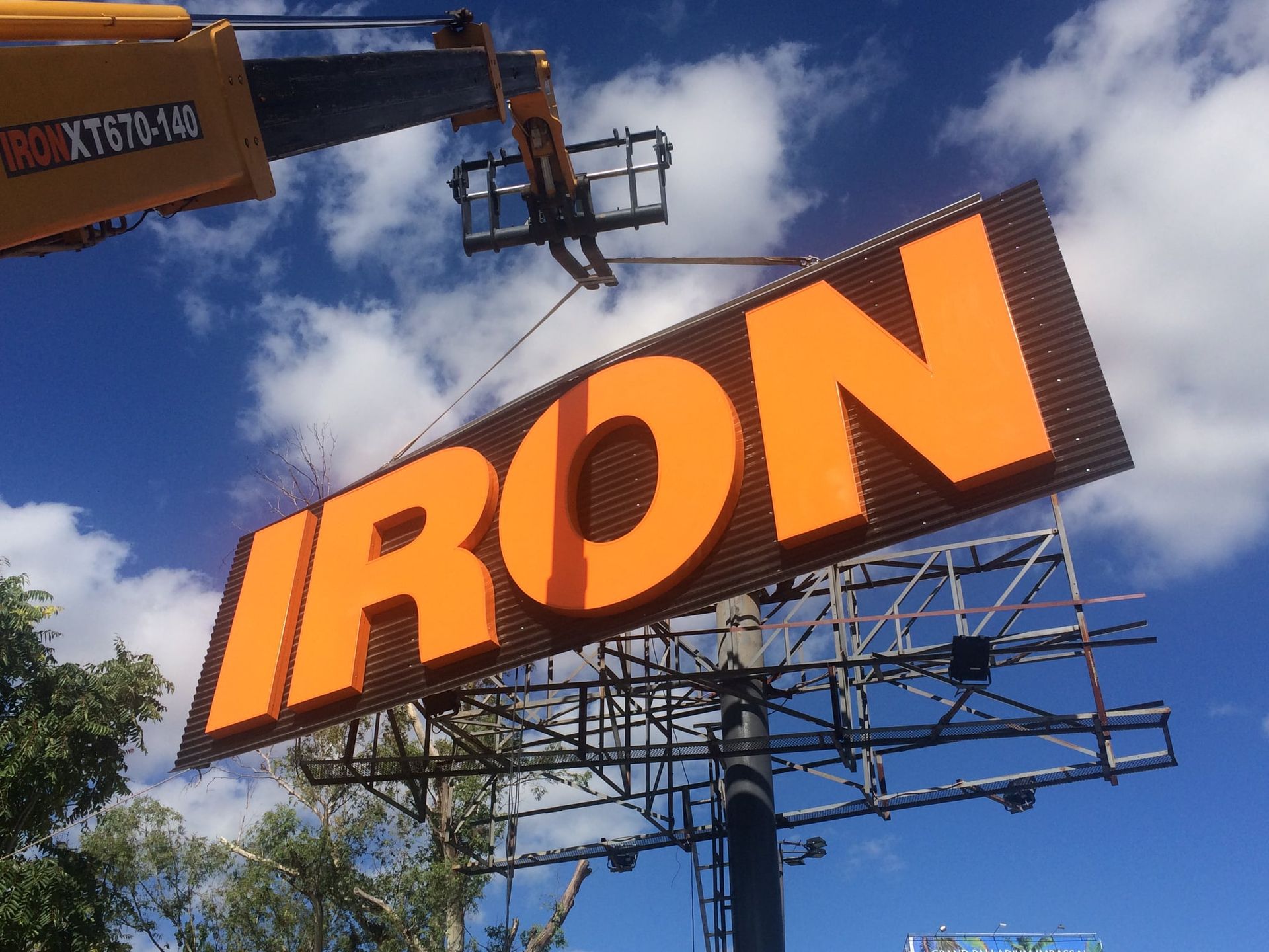 Una grúa levanta un gran cartel naranja que dice 