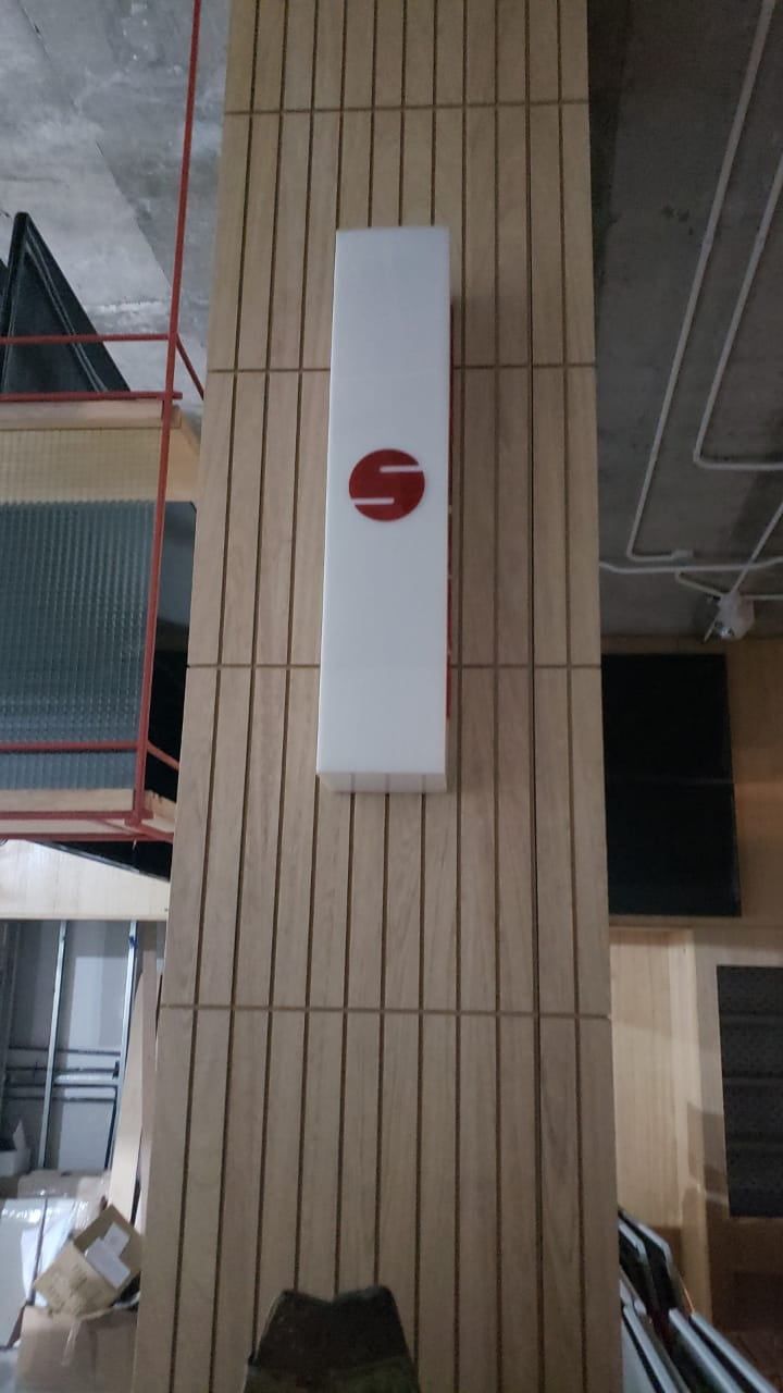 Letrero blanco con logotipo en forma de remolino rojo montado sobre un pilar revestido de madera 