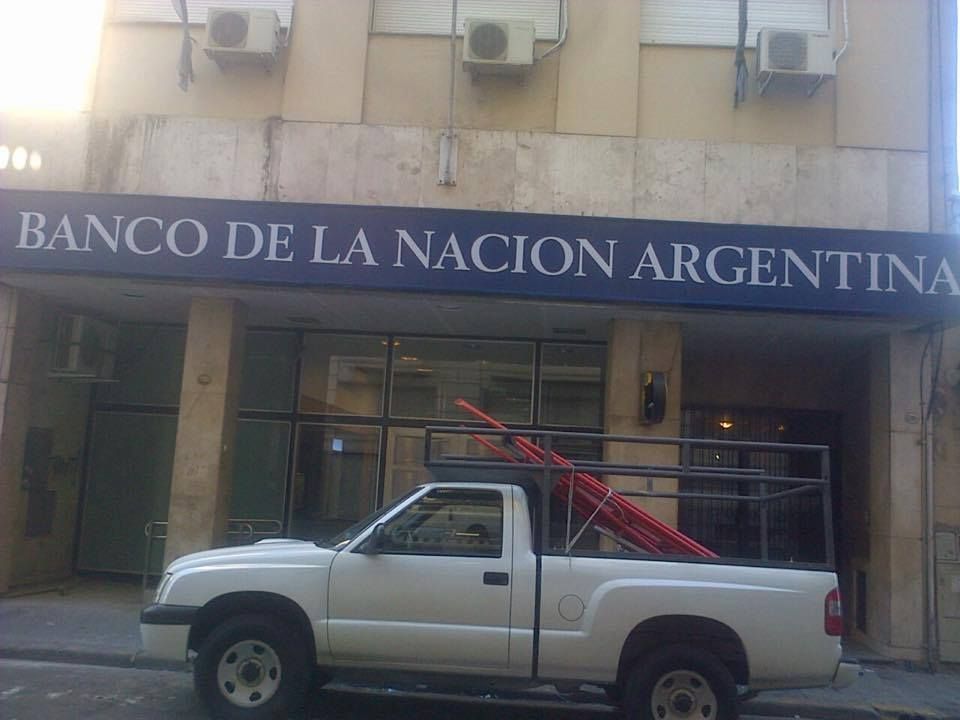 Camioneta blanca estacionada frente al edificio del Banco de la Nación Argentina, caños rojos en la caja.