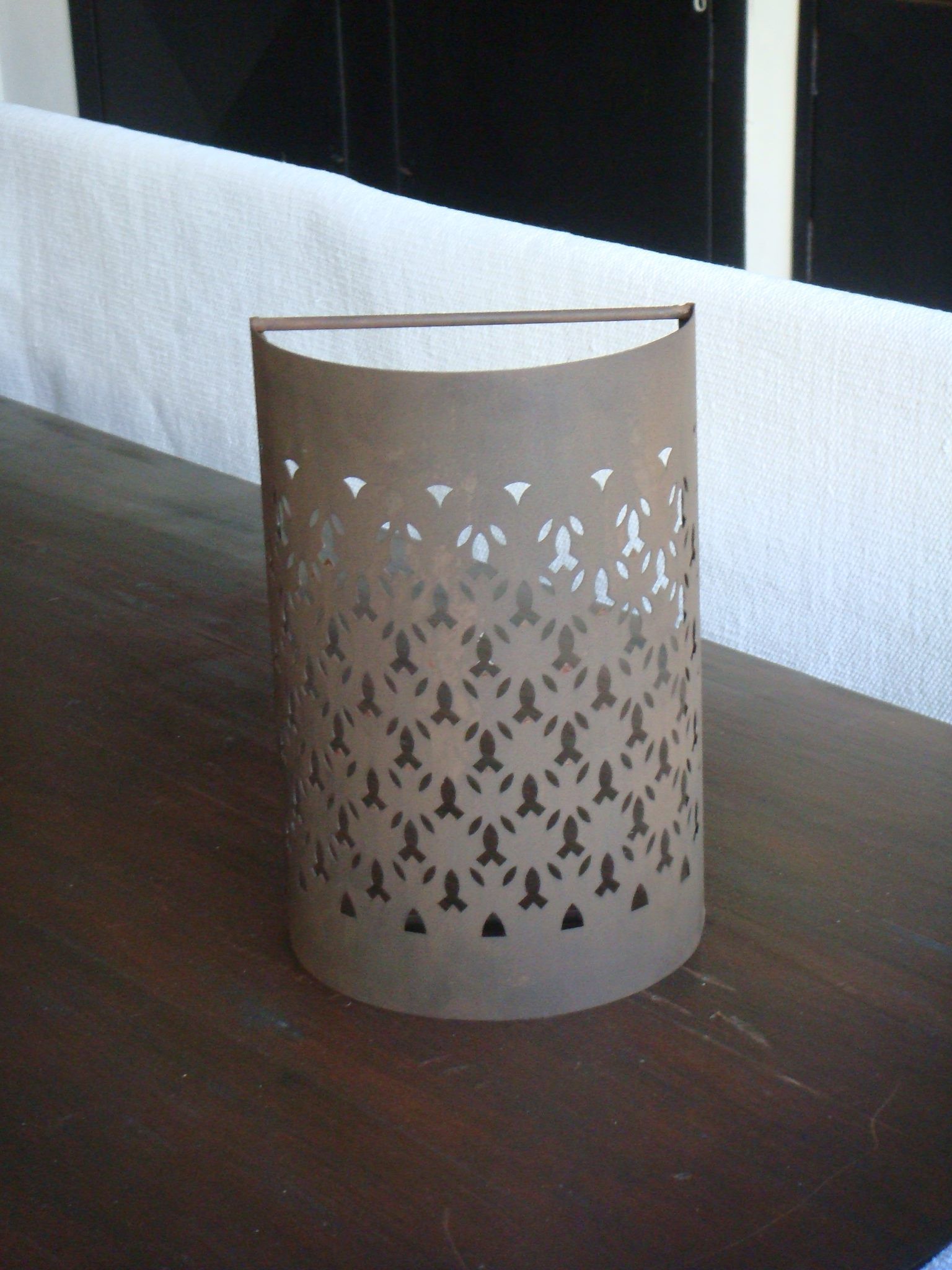 Portavelas de metal marrón con diseño geométrico recortado sobre una mesa de madera oscura.