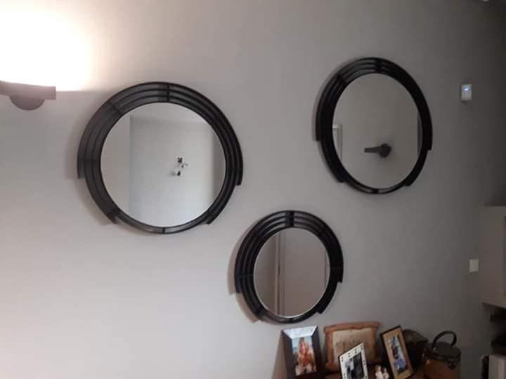 Tres espejos circulares con marco negro y de distintos tamaños sobre una pared gris