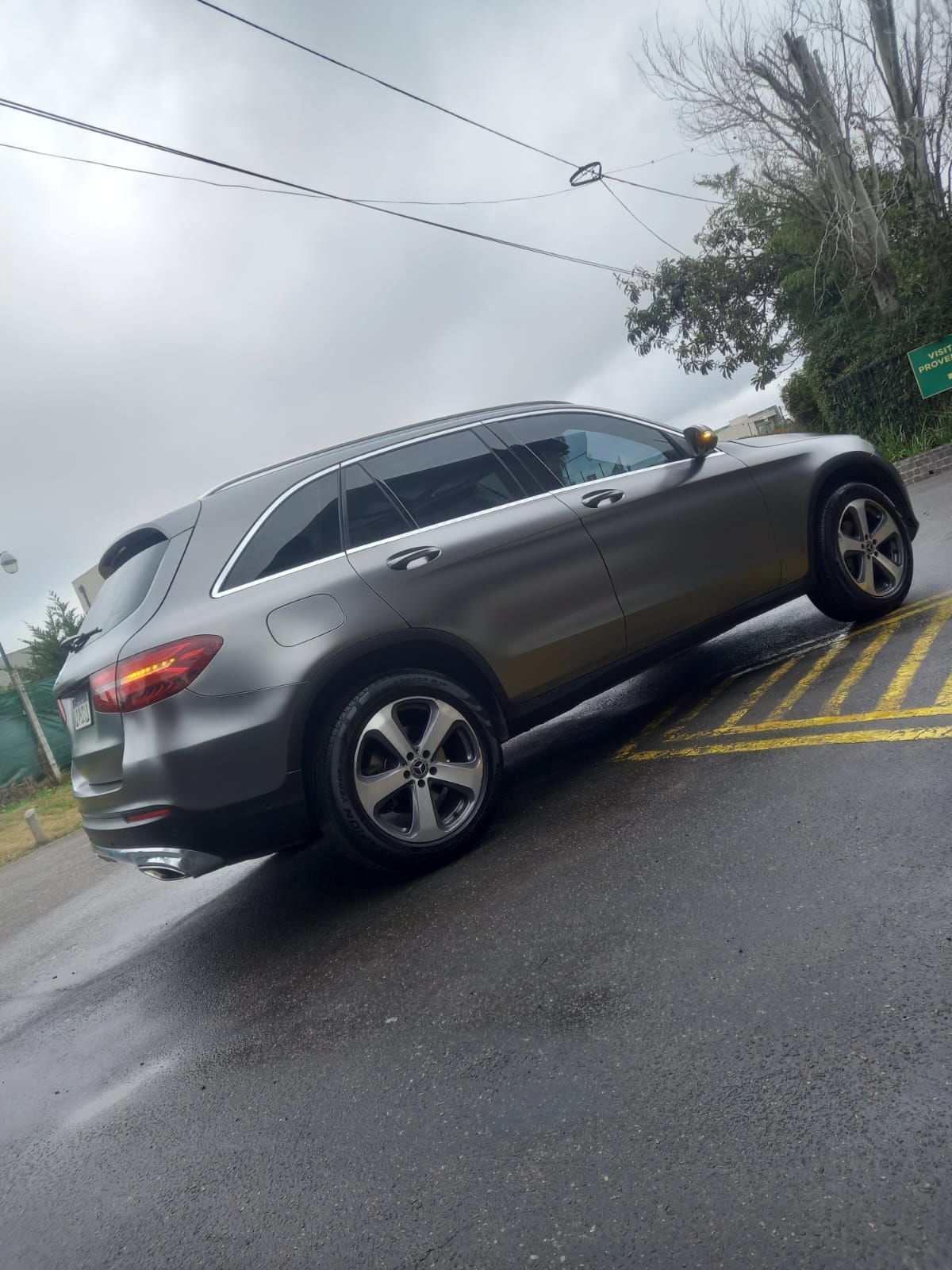 Un todoterreno Mercedes-Benz gris estacionado sobre asfalto mojado. Cielo nublado.