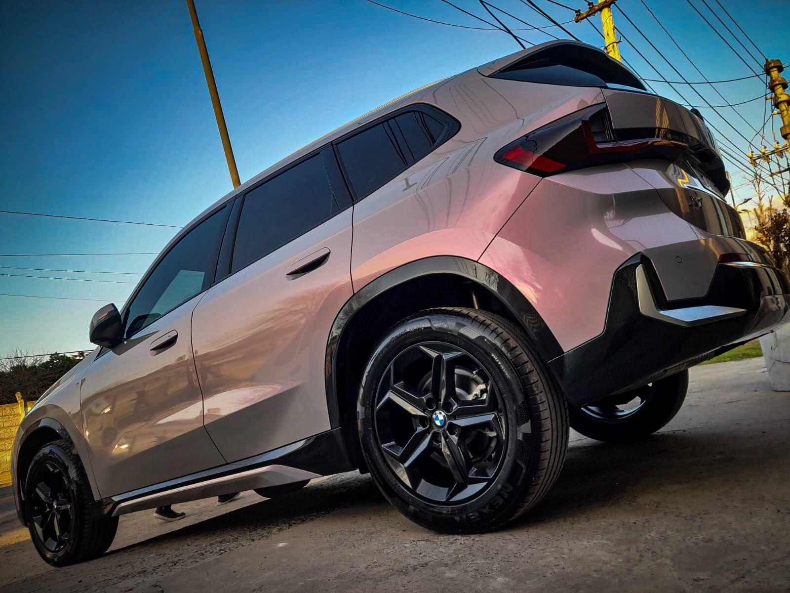 Un moderno SUV BMW de color rosa metalizado estacionado en una carretera pavimentada