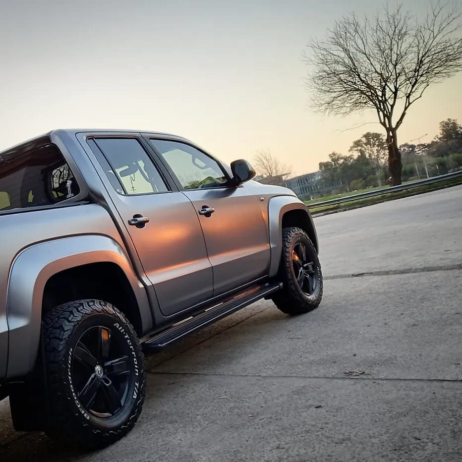 Camioneta gris estacionada sobre asfalto; árbol desnudo al fondo, puesta de sol.