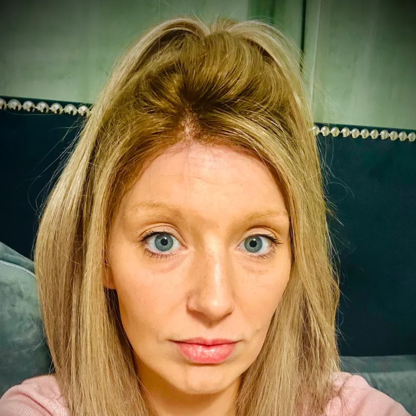 Woman with blonde hair and blue eyes, looking at the camera. She's in front of a blue couch.