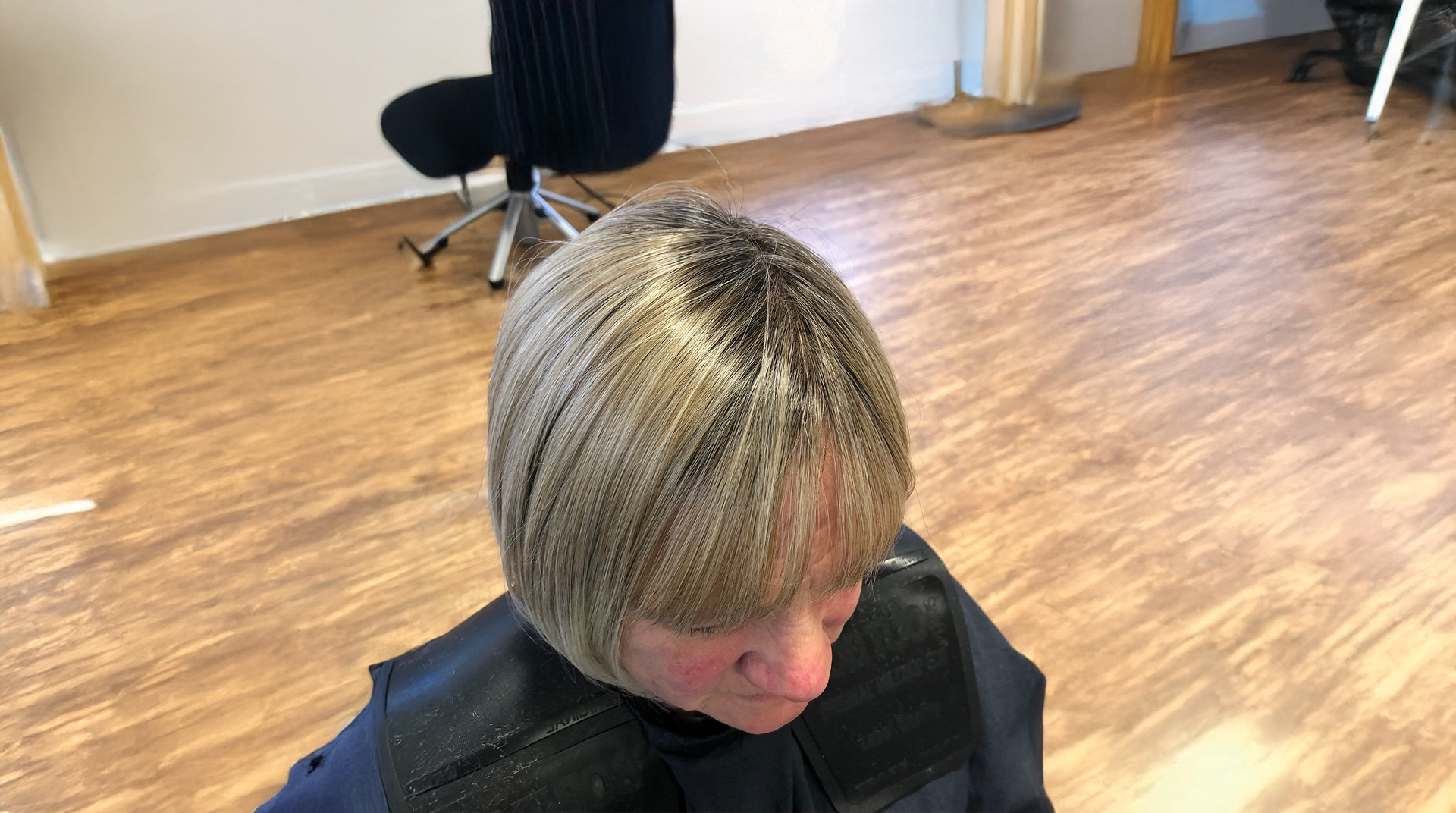 Person with a short, layered bob haircut, blonde with dark roots. Sitting in a salon chair.