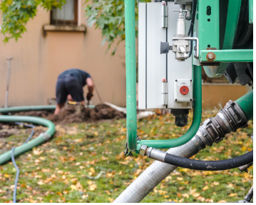 A man is digging in the dirt next to a green hose.