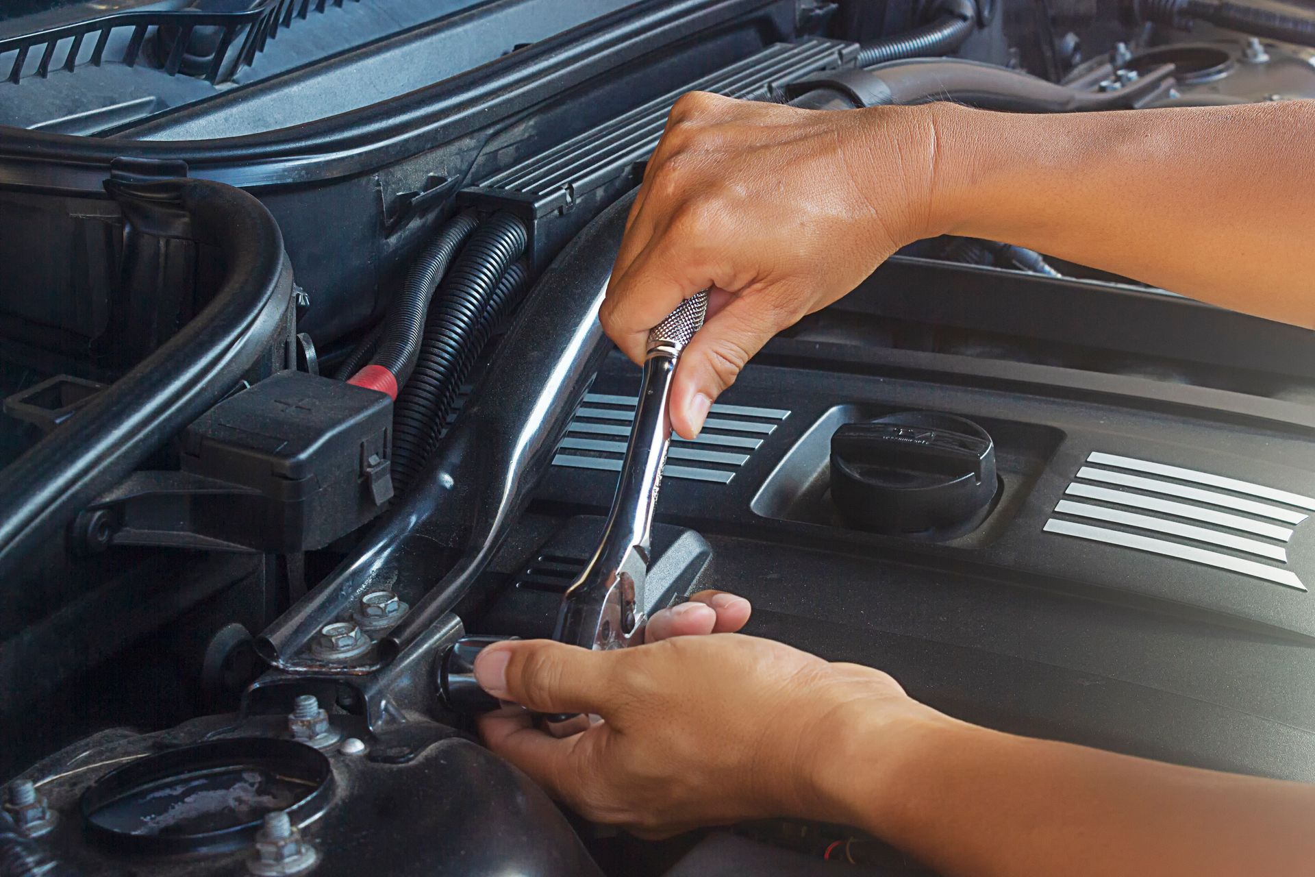 A person is working on the engine of a car with a wrench.