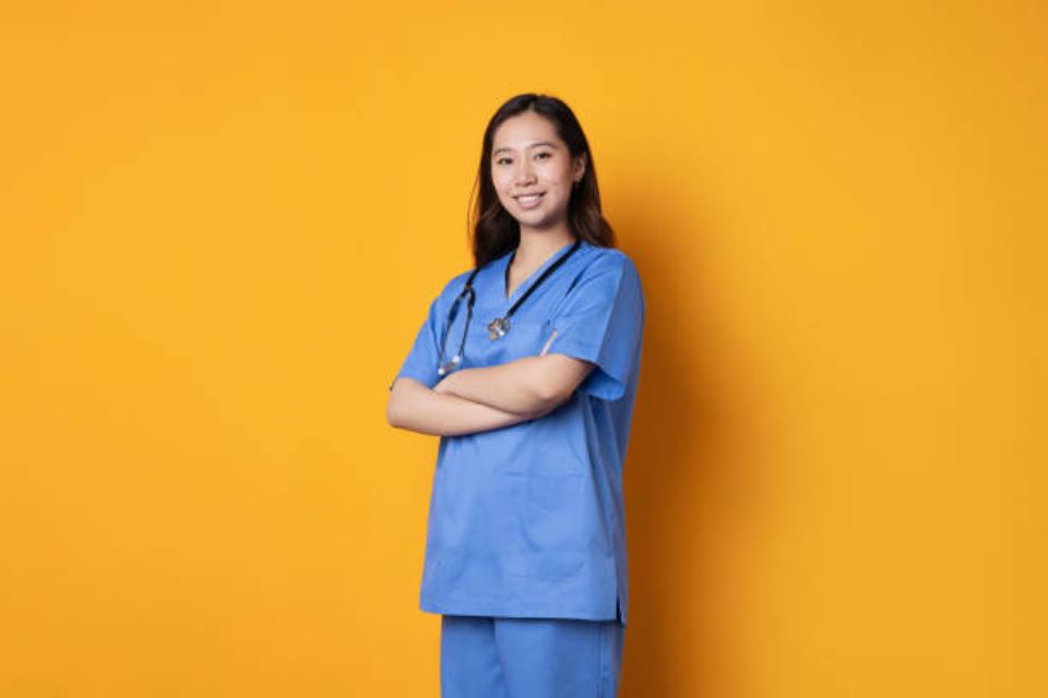 smiling female doctor in lab coat with arms crossed against yellow background