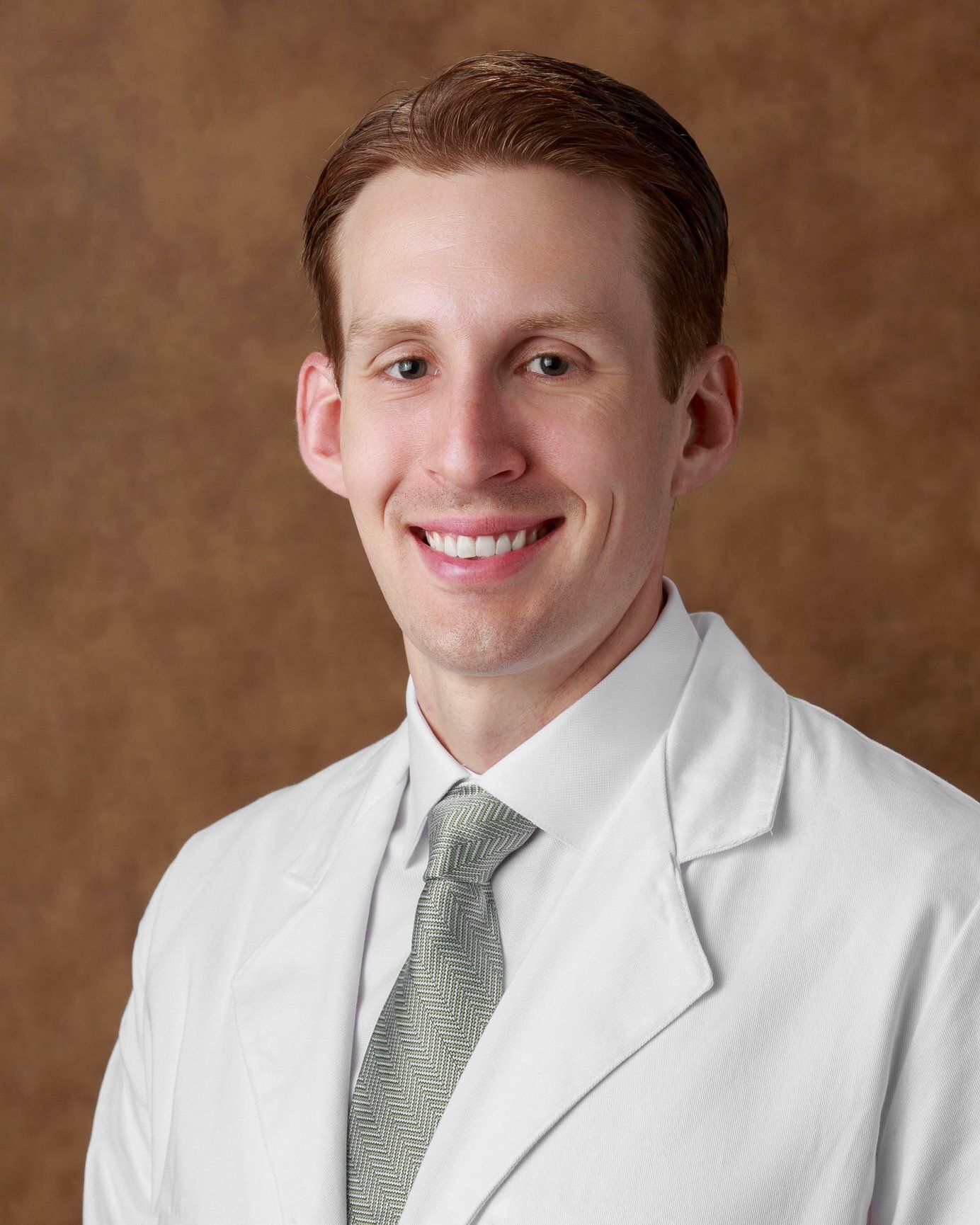 A man in a white coat and tie smiles for the camera