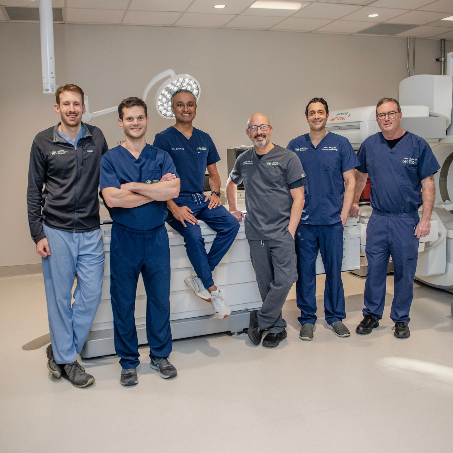 A medical team in scrubs stands in an examination room. They pose near a large medical machine.
