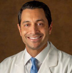 A man in a white coat and blue tie is smiling for the camera.