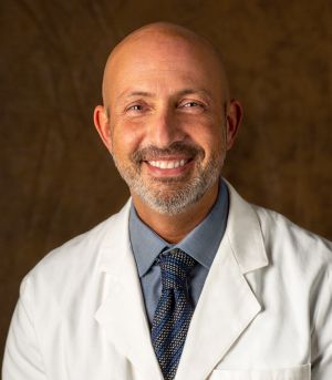 A bald man with a beard is wearing a white coat and tie.