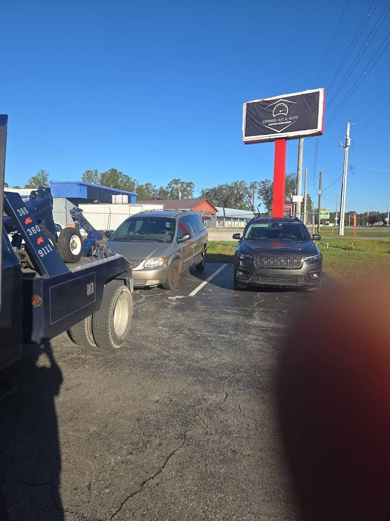 A tow truck is hooking up a minivan parked beside a black car on a sunny day.