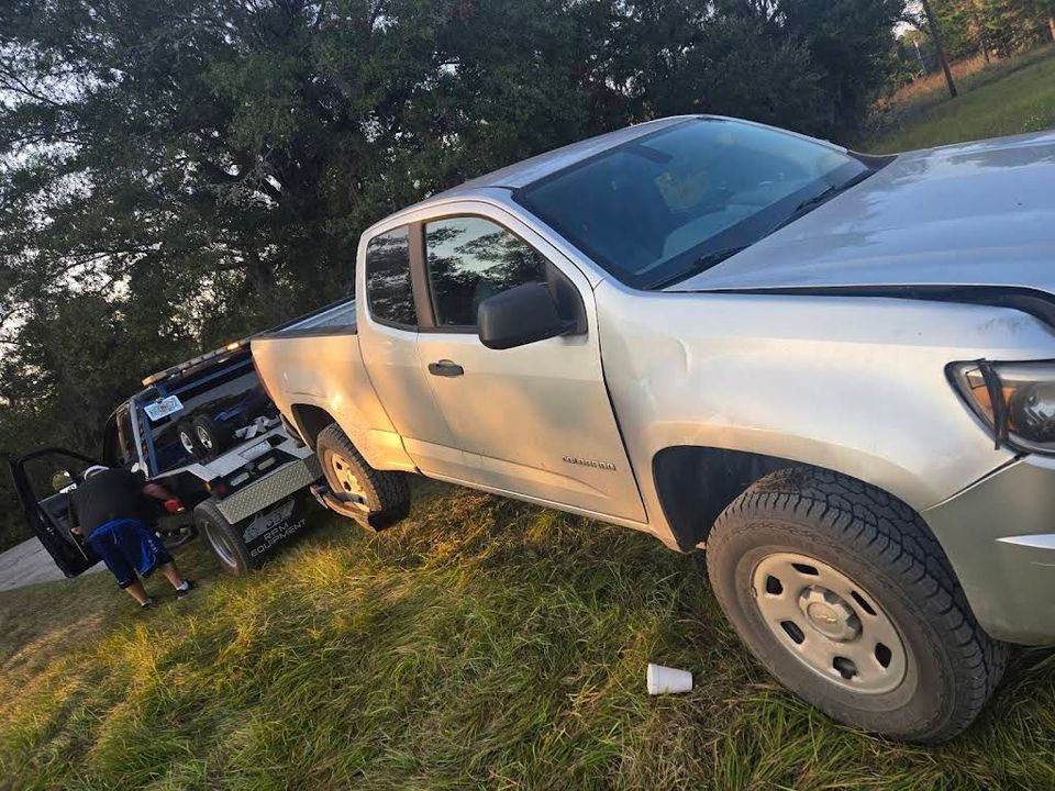 Silver truck on grass; another vehicle behind it, person near the truck.