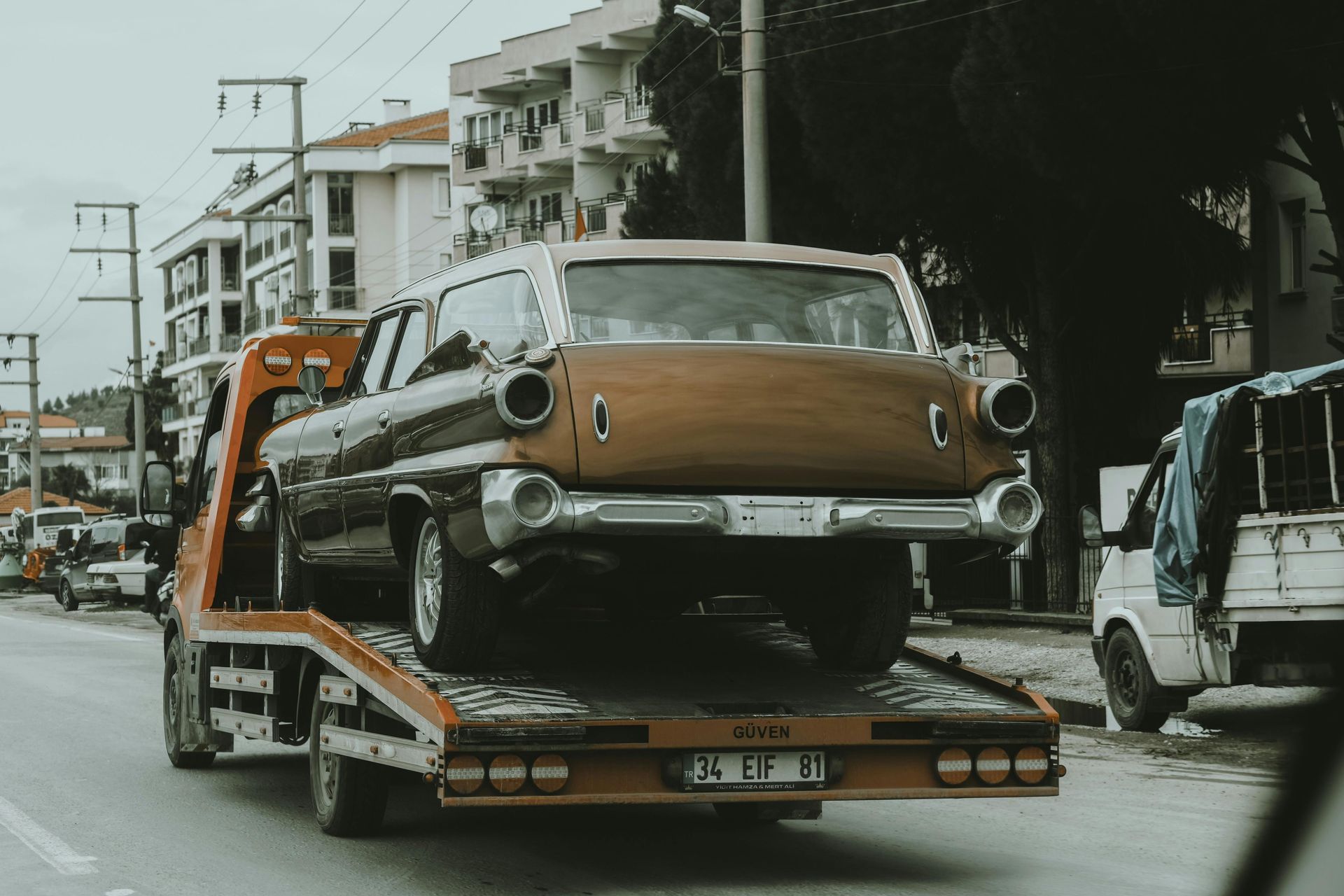 A vintage station wagon on a tow truck, brown and black exterior, on a city street.