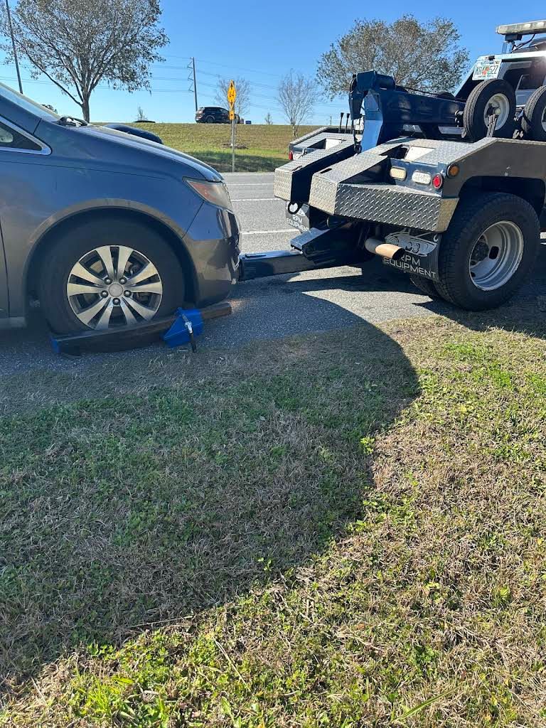 A gray car being towed by a tow truck, parked on grass next to a road.