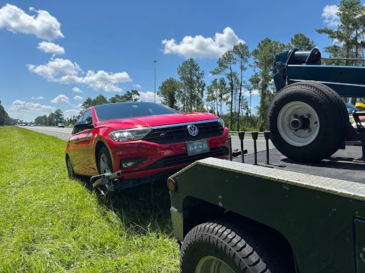 A red Volkswagen Jetta being towed by a tow truck on the side of a road.