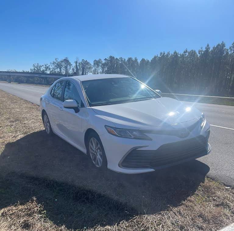 White Toyota Camry parked on the side of a road with a sunny sky.