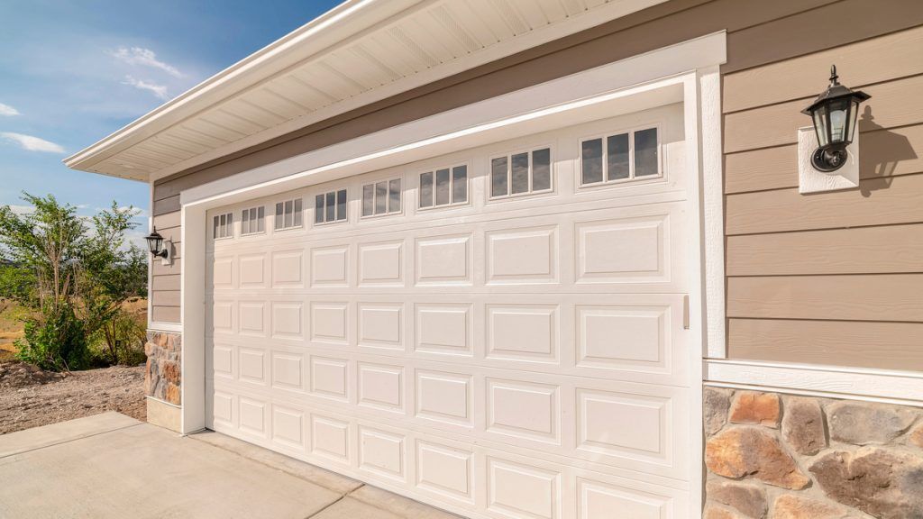 White garage door with windows, tan siding, and stone accents.