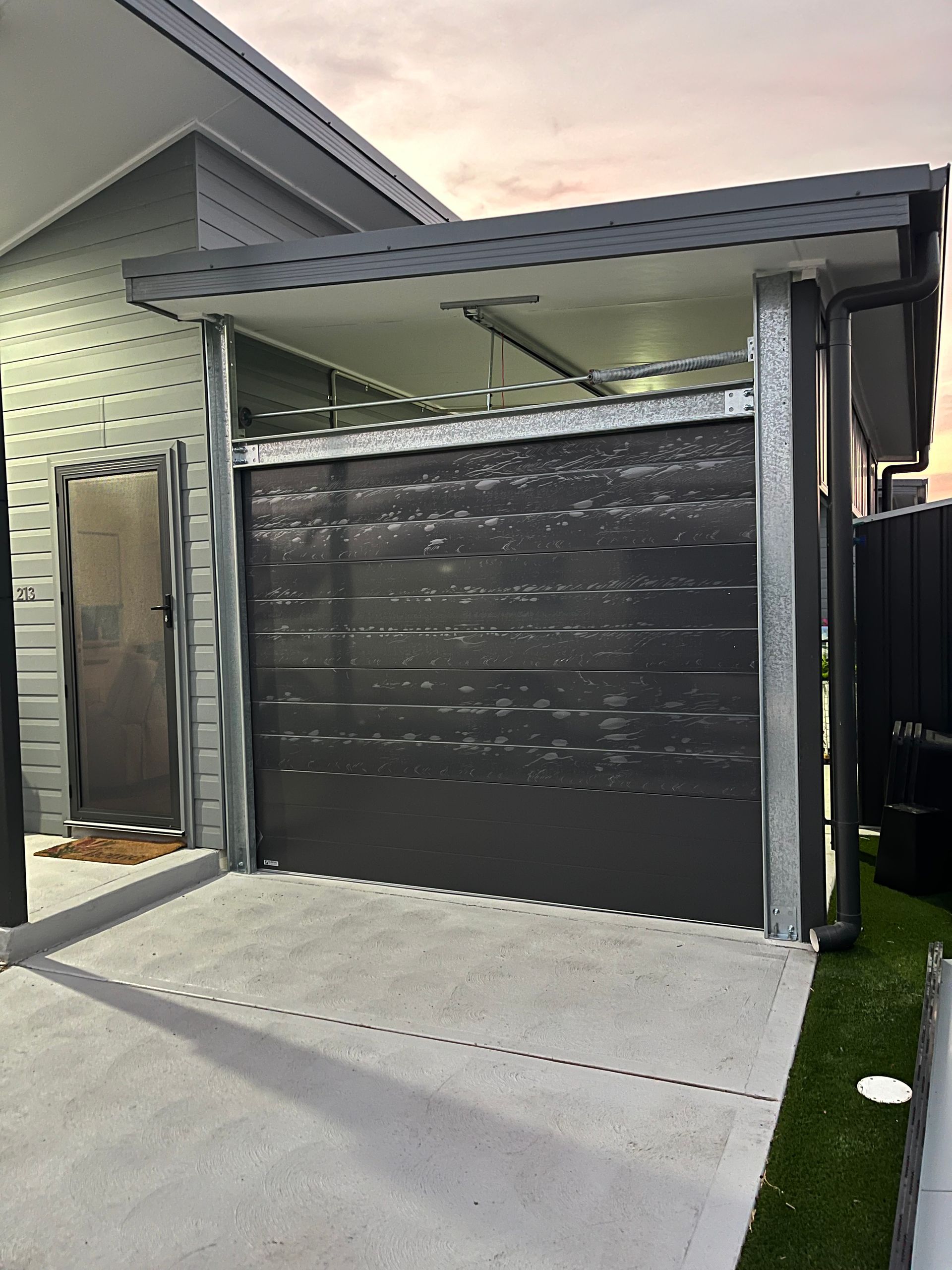 Modern garage with a black roller door and a concrete driveway beside a house.