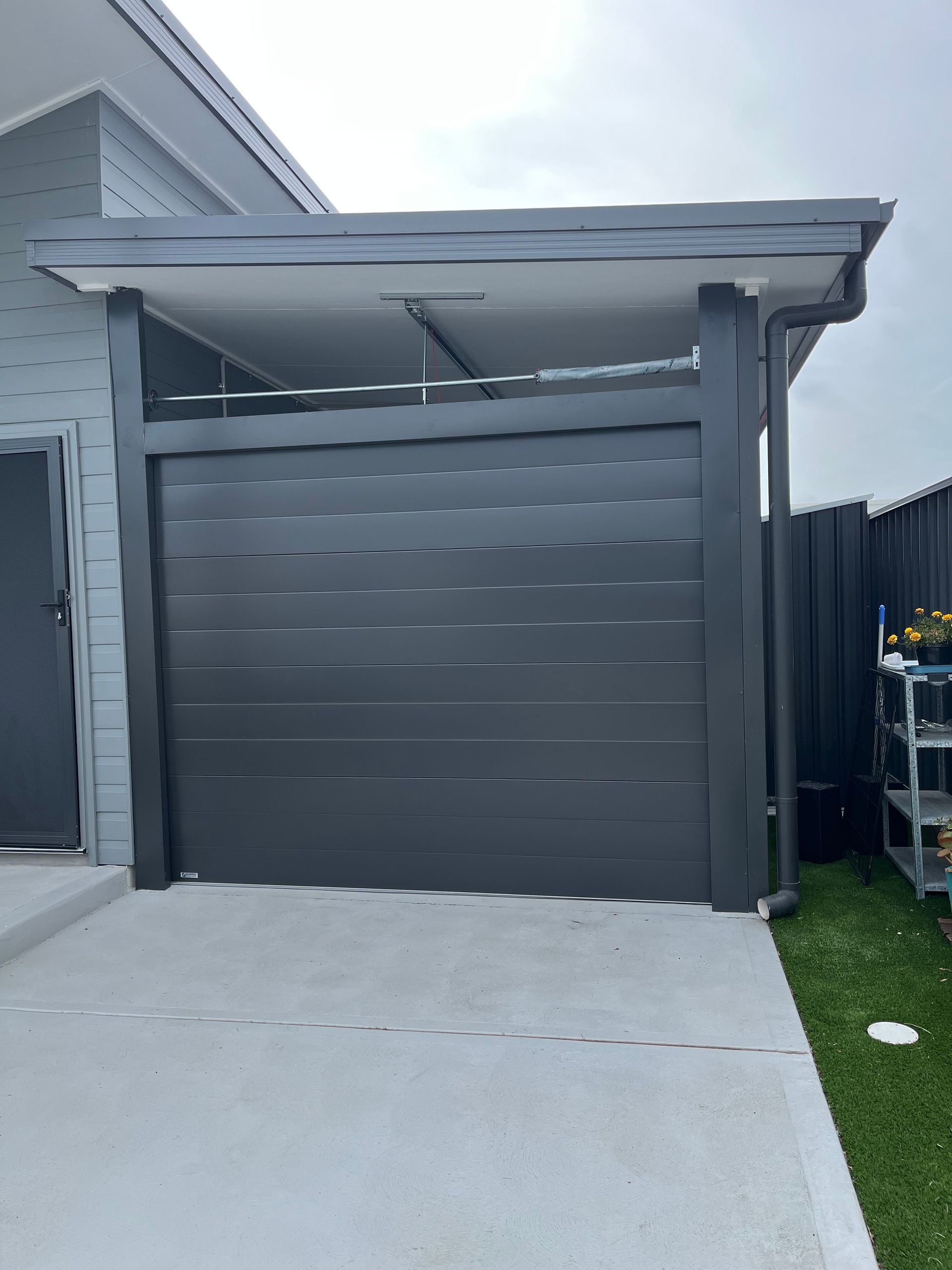 Gray garage with a covered driveway and a white house exterior beside it.