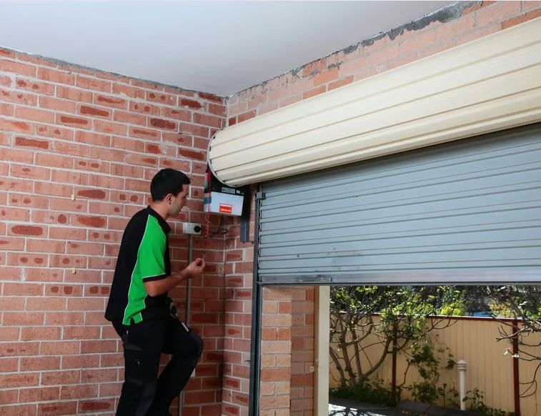 Man working on a rolling garage door, brick wall background.