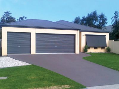 Tan house with dark gray garage doors and driveway, green lawn.