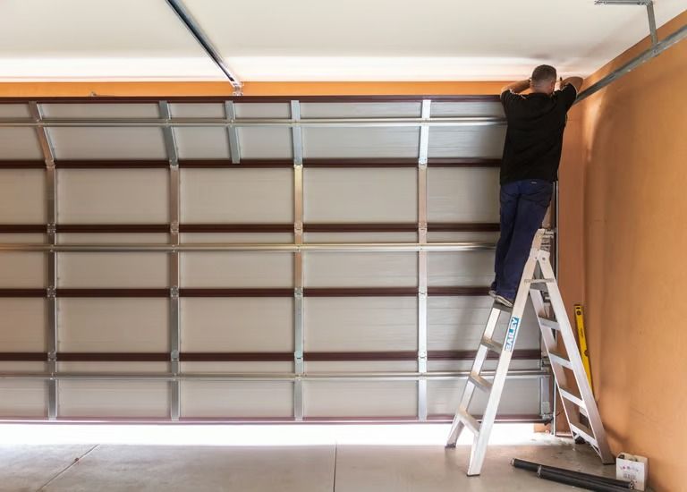 Man on ladder installing garage door frame, working in a garage.