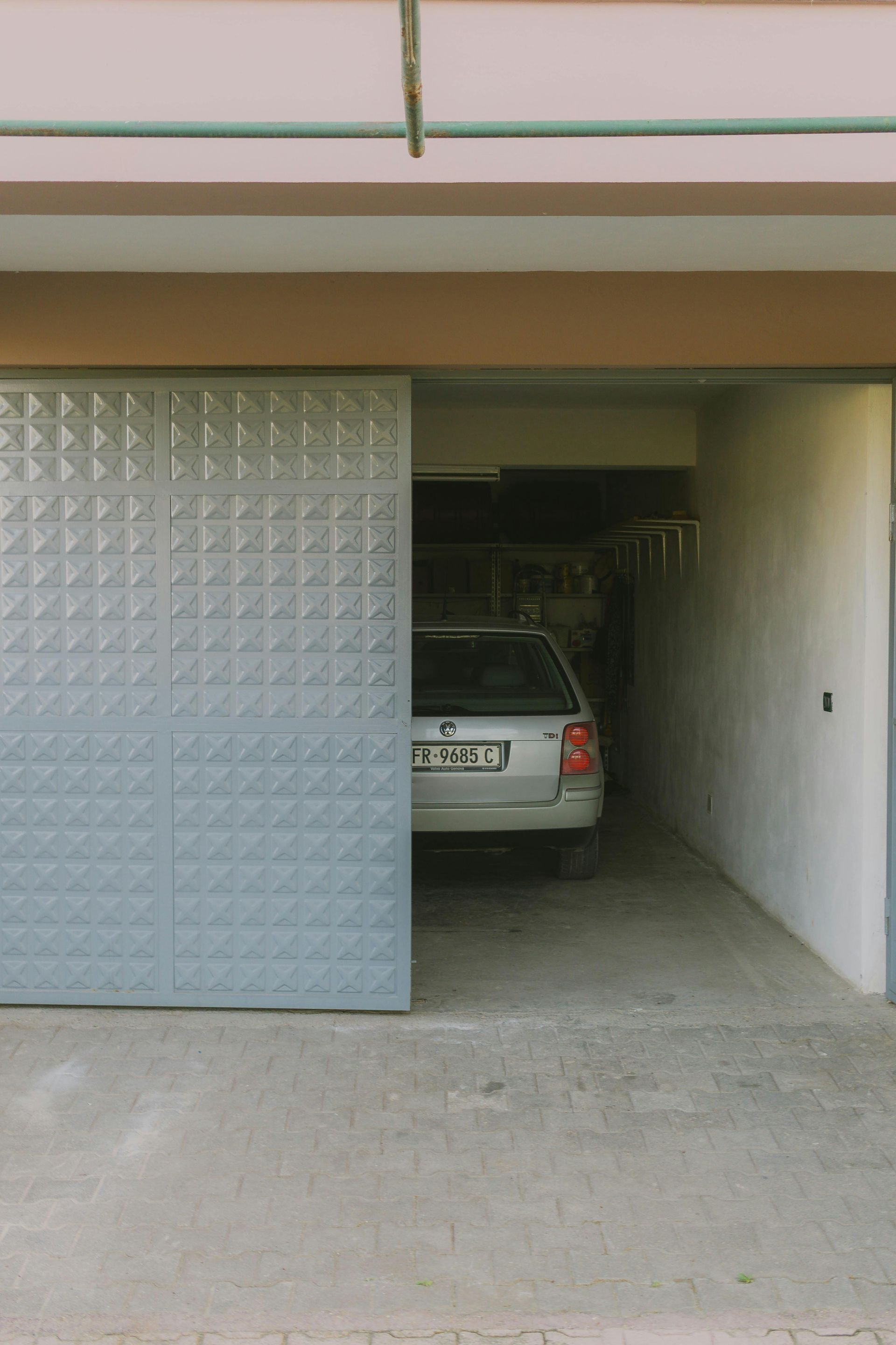 Car parked inside a narrow garage with a partially open metal door.