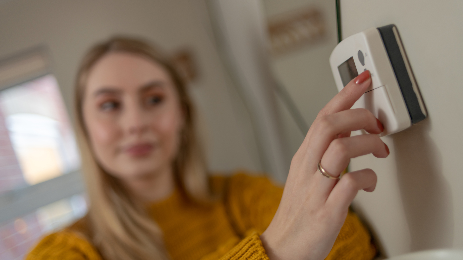 A woman is adjusting a thermostat on a wall.