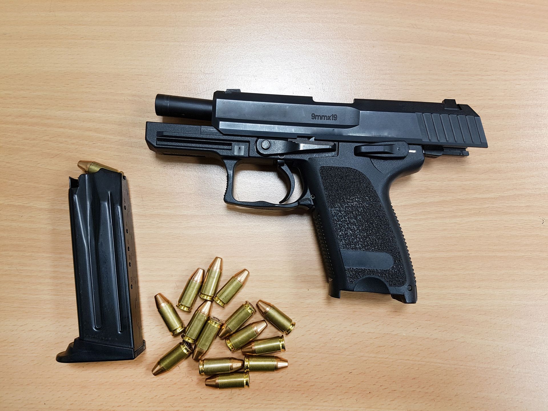 Black handgun with open slide, magazine, and ammunition on a wooden surface.