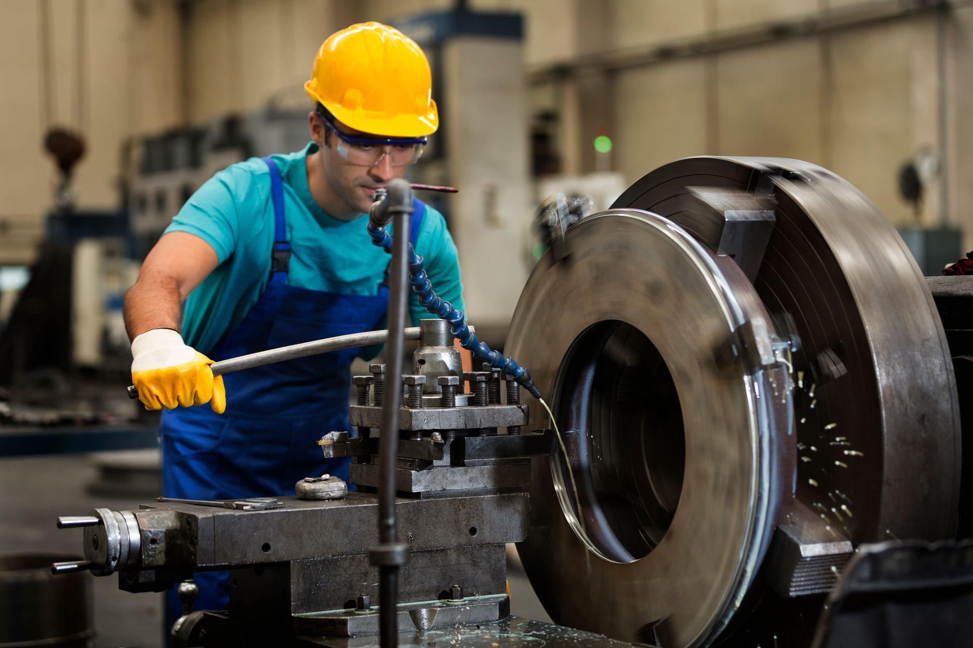A male professional metal fabricator with yellow protective hat and gloves at a factory.