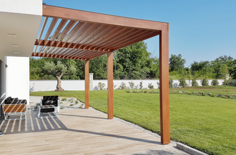 A wooden pergola is sitting on top of a patio next to a lush green field.