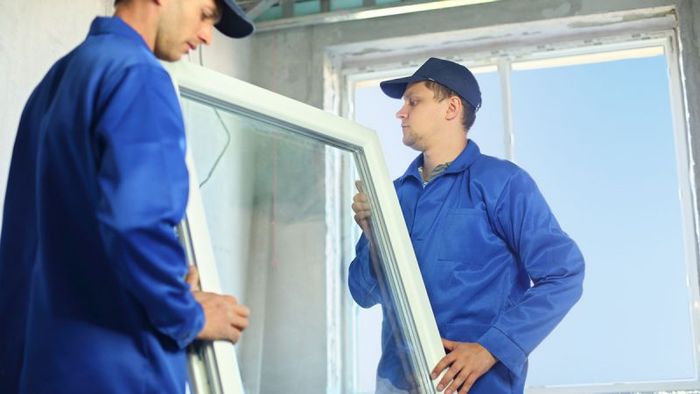 Two men are installing a window in a room.