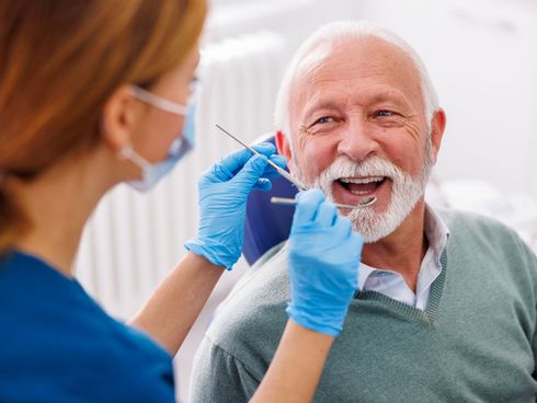 An elderly man is having his teeth examined by a dentist.
