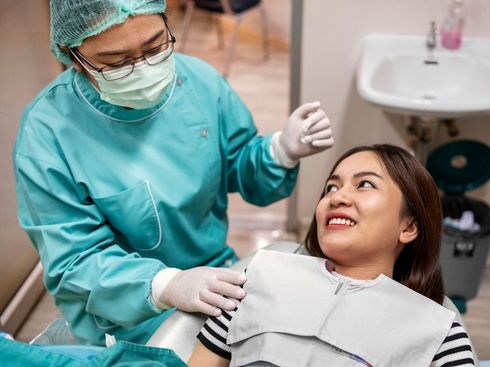 A woman is sitting in a dental chair while a dentist examines her teeth.