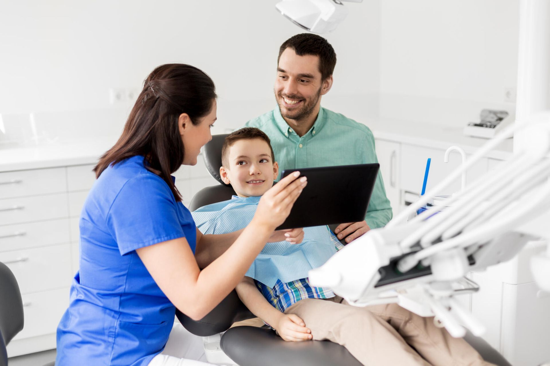 Dentist showing a young patient and father a tablet in a dental office.