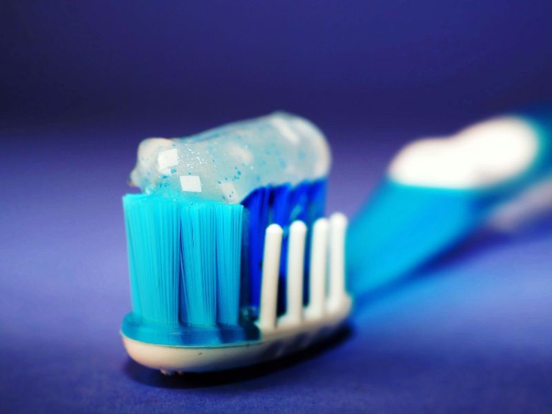 A blue toothbrush with toothpaste on it on a blue surface.