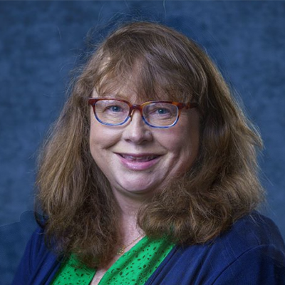 A woman wearing glasses and a green shirt is smiling for the camera.