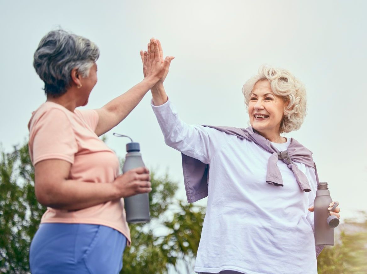 Two older women are giving each other a high five while holding water bottles.