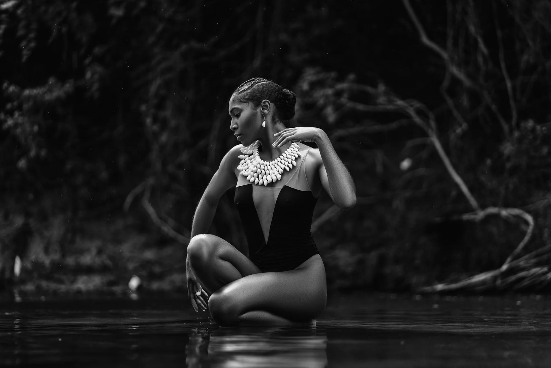 A black and white photo of a woman in a swimsuit kneeling in the water.