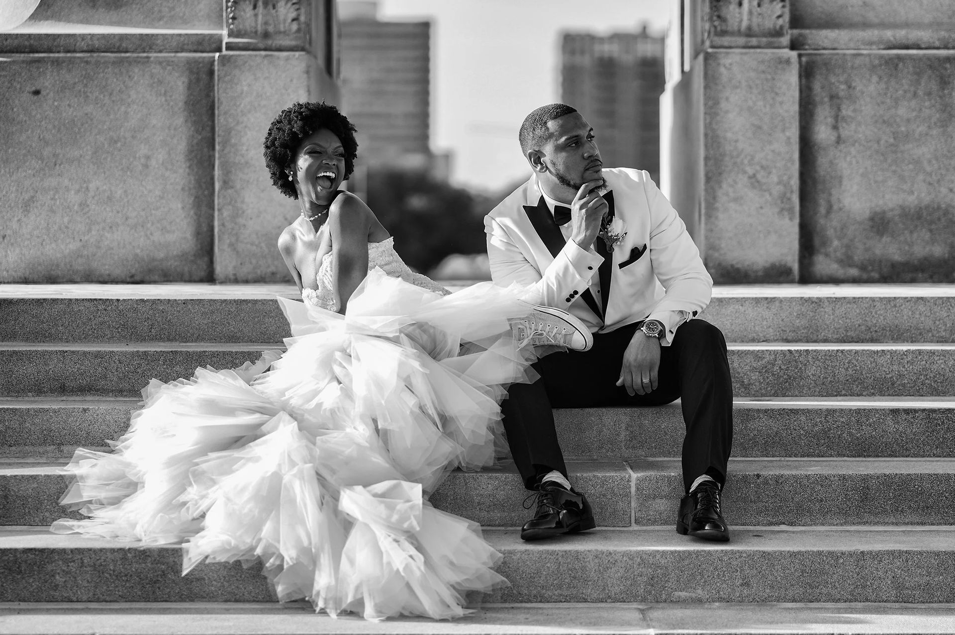 A black and white photo of a bride and groom sitting on stairs.