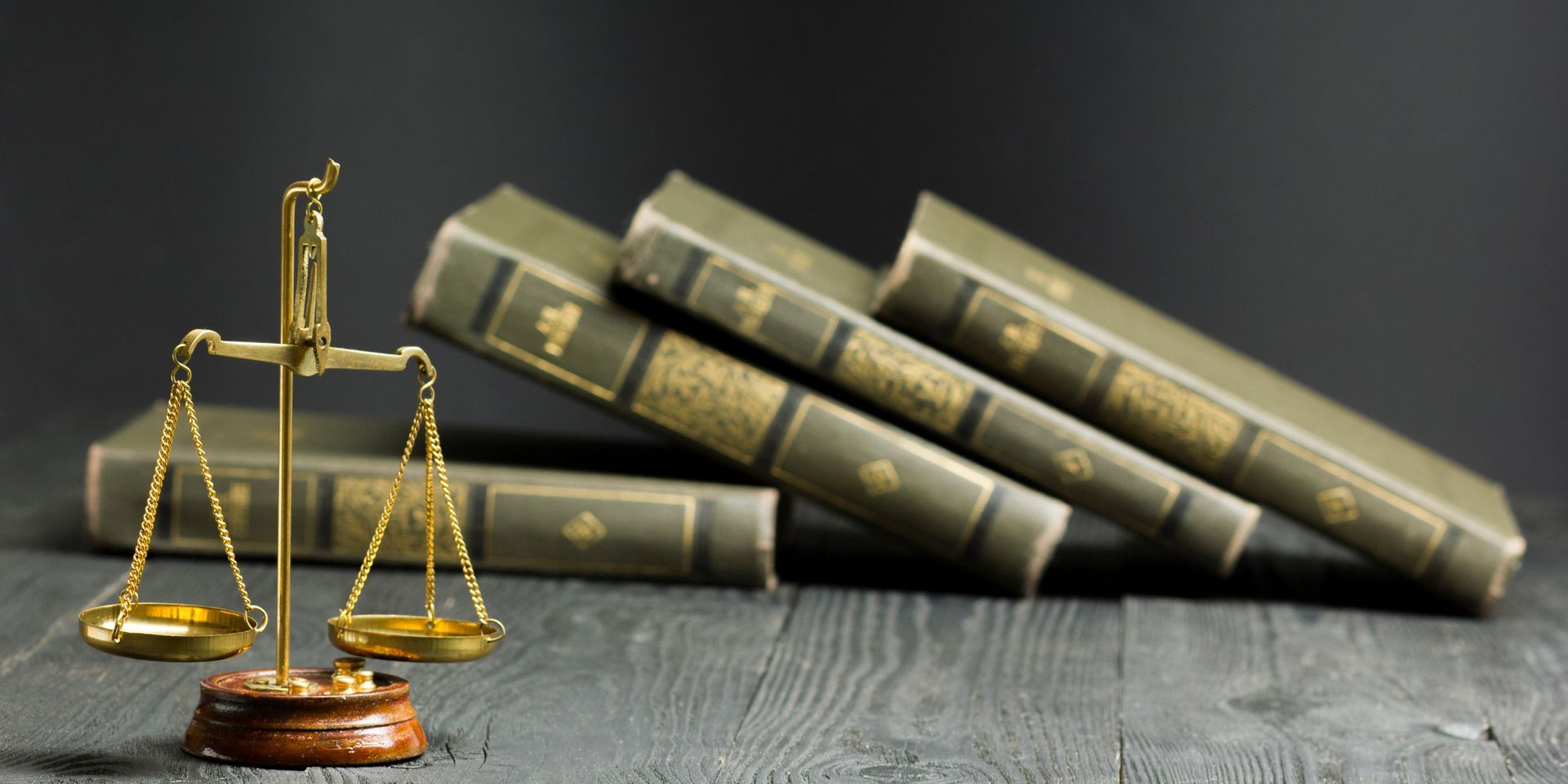 A scale of justice is sitting on a wooden table next to a stack of books.