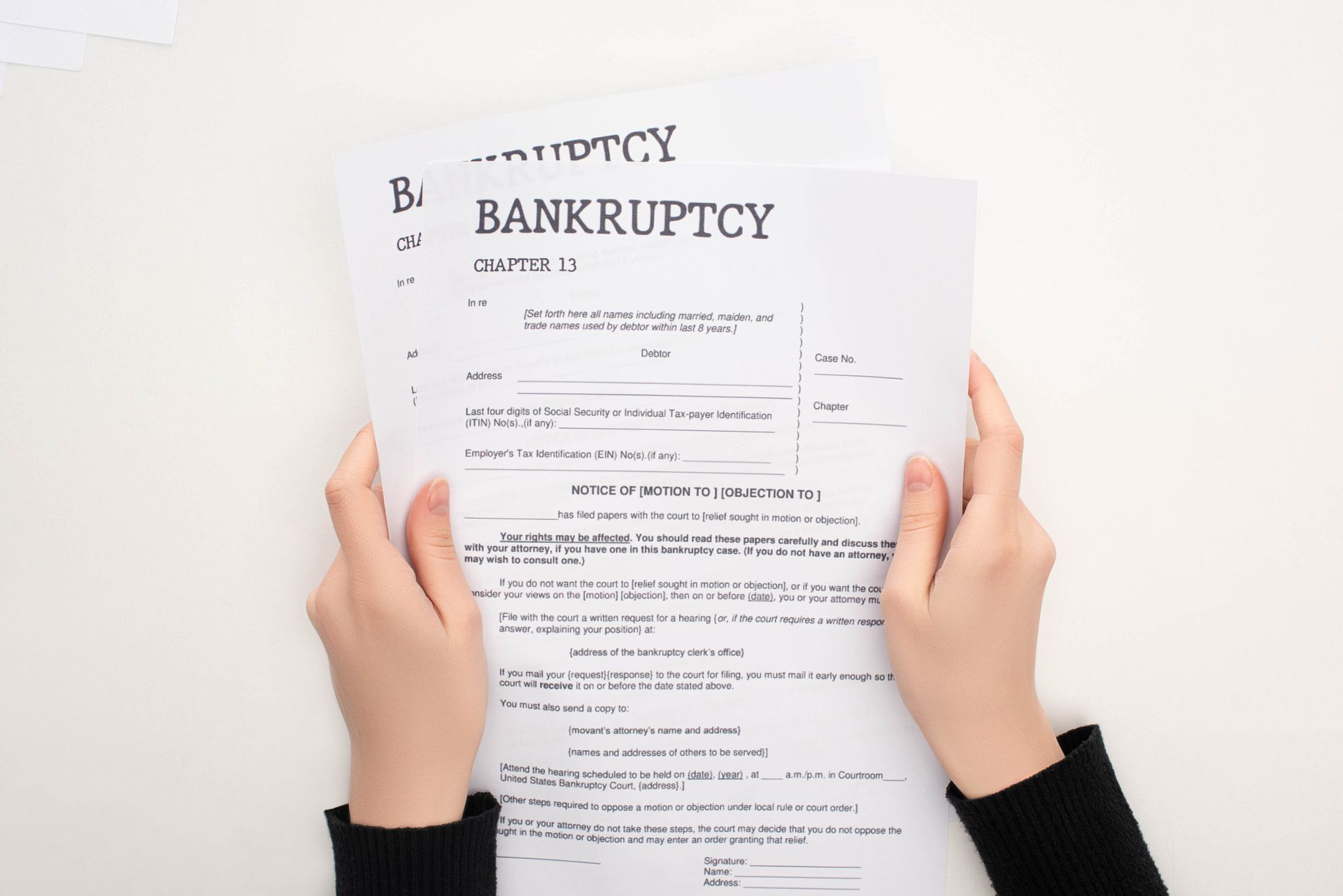 Hands in dark sleeves hold a printed bankruptcy petition form against a plain white background.
