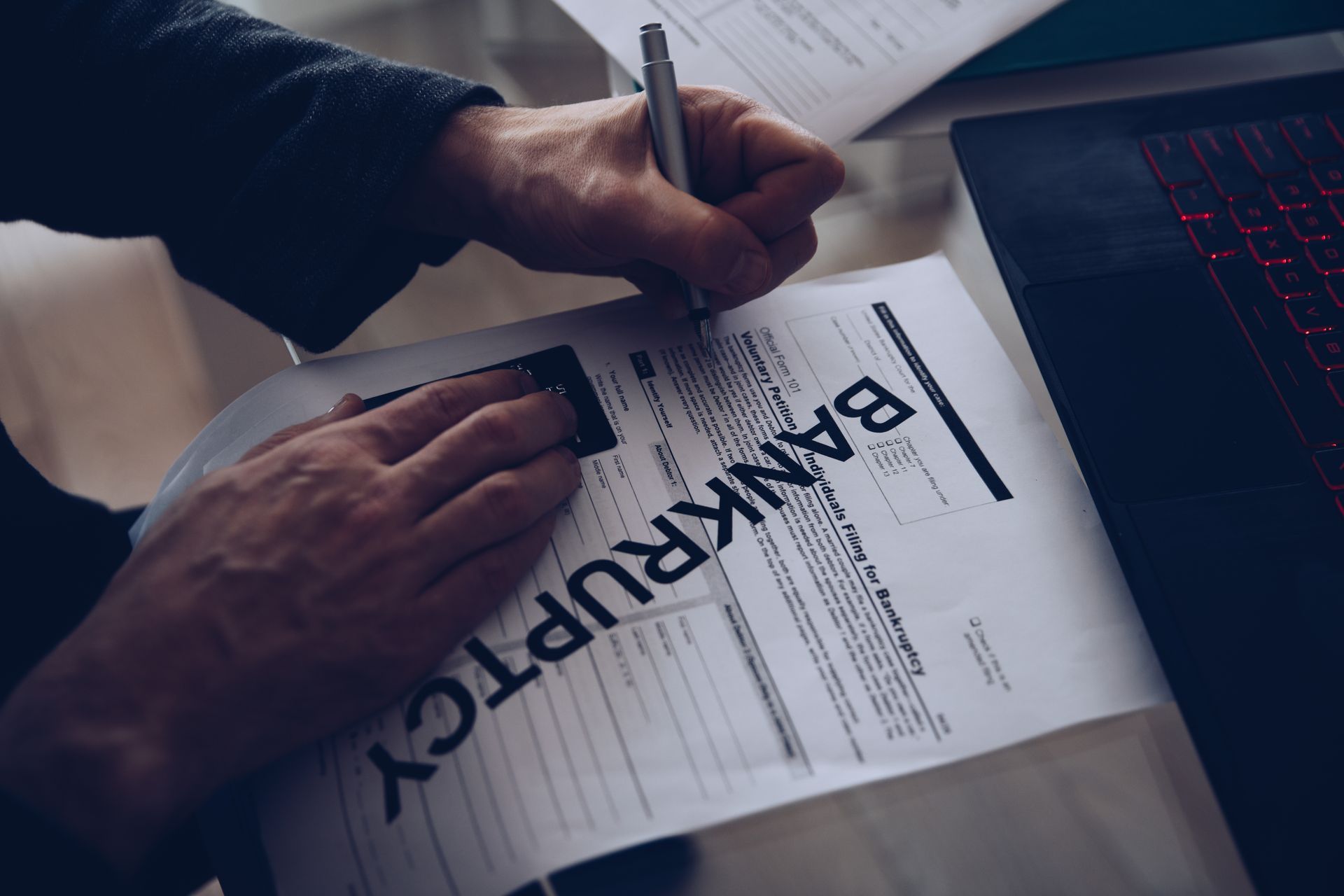 Person writing on bankruptcy paperwork at a desk next to a laptop.