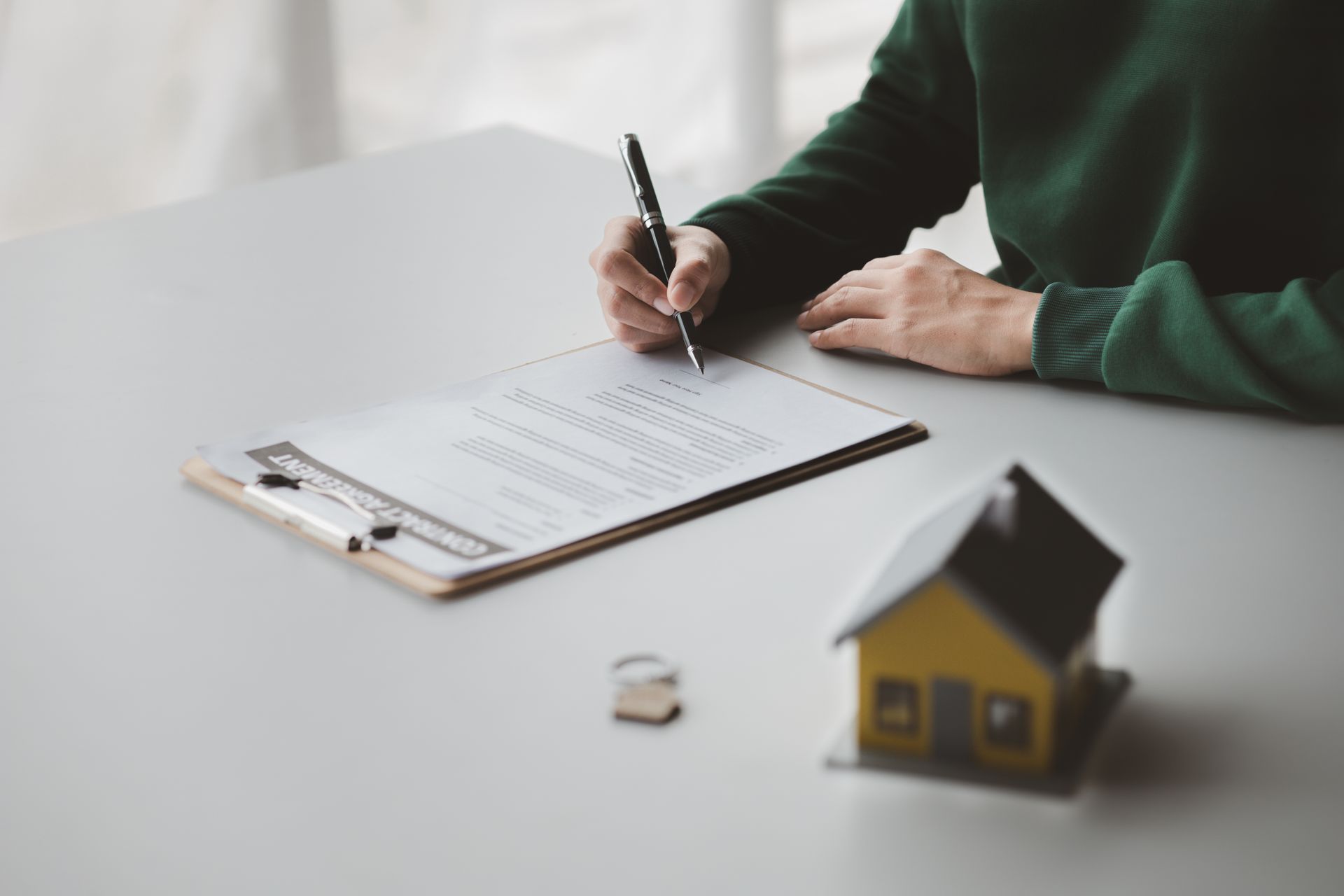 A person is sitting at a table writing on a clipboard next to a model house.